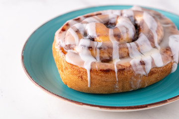 Large gourmet frosted cinnamon roll on marble table.