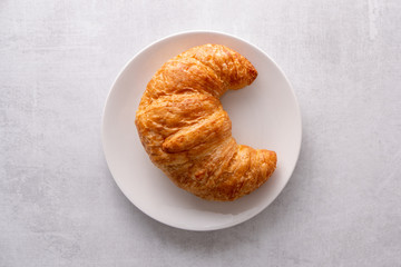 Warm crispy flaky croissant roll on white plate and distressed table.