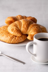 Warm crispy flaky croissant roll on white plate and distressed table.
