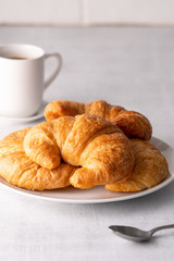 Warm crispy flaky croissant roll on white plate and distressed table.