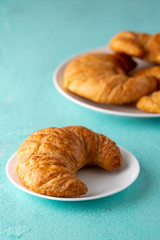 Warm crispy flaky croissant roll on white plate and distressed table.