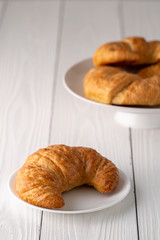 Warm crispy flaky croissant roll on white plate and distressed table.