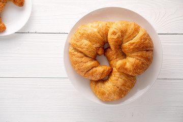 Warm crispy flaky croissant roll on white plate and distressed table.