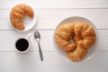 Warm crispy flaky croissant roll on white plate and distressed table.