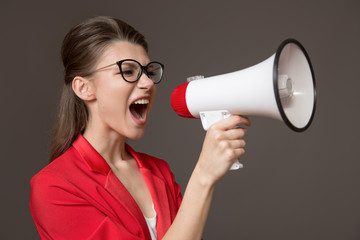 Naklejka premium business woman shouting at a megaphone. Young pretty girl in glasses and a red jacket