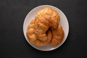 Warm crispy flaky croissant roll on white plate and distressed table.