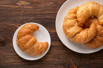Warm crispy flaky croissant roll on white plate and distressed table.