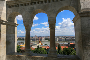 Beautiful view of the city and the Hungarian parliament building through the wall and arches of the Fisherman's Bastion on a sunny summer day in Budapest, Hungary