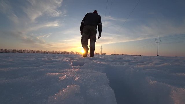 male worker in warm clothes and warm boots goes on a cold winter day in the snow along the power line at sunset and looking something.