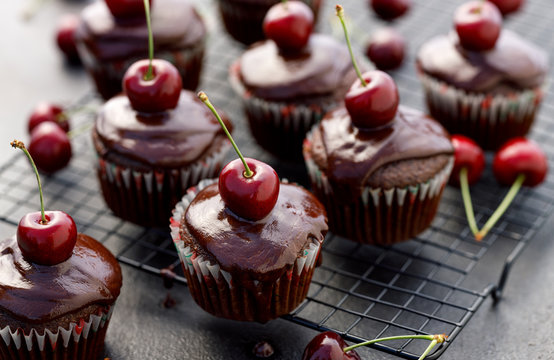 Cherry-Chocolate-coffee muffins with melted dark chocolate topping with the addition of fresh cherries on on a cooling tray, on a dark background, close-up. Delicious dessert