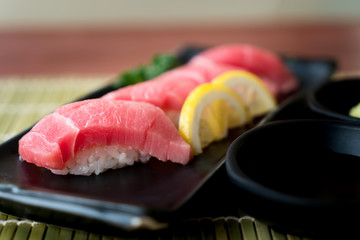 Otoro tuna sushi on black plate along with Japanese sauce and green leaf decoration, Japanese food, close up at sushi ..