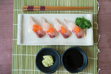 Hamachi sushi on white plate along with Japanese sauce and green leaf decoration, Japanese food, Top view at sushi.