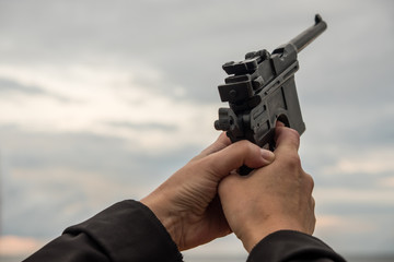 Hand with a gun against the sky, clouds. Life-size weapons mockup. Summer evening.