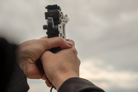 Hand with a gun against the sky, clouds. Life-size weapons mockup. Summer evening.