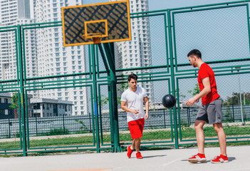 Two guys playing basketball after each-other on the court in the middle of the day