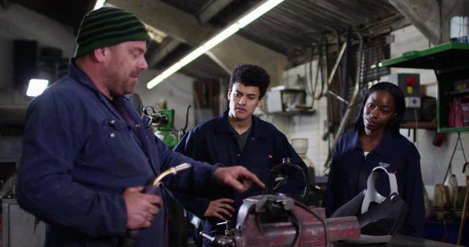4K Young apprentices learning from experienced mechanic in auto repairs shop. Slow motion.