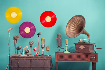 Old retro microphones, antique gramophone phonograph turntable with brass horn, flying multicolor LP vinyl record discs front blue background. Nostalgia music concept. Vintage style filtered photo