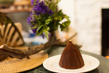 Chocolate Cake in pyramid mountain shape with choc powder on top over stylish western house and oven fire, Tasty and sweet bake bakery on plate with flower