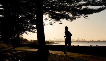Early morning jogger silhouetted against the skyline of the distance city of Melbourne, Australia.
