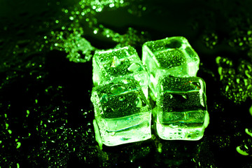Green ice cubes on black wet table.