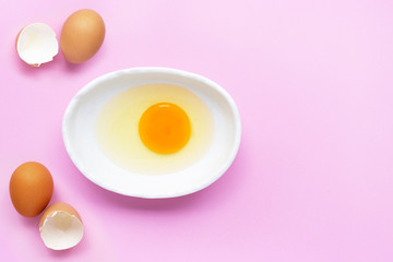 Egg yolk and white in a bowl on pink background.