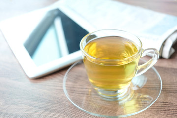Cup of green tea hot on the desk has a newspaper and a tablet. at office