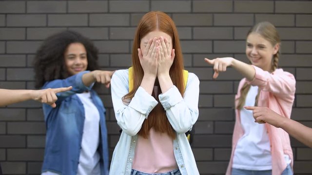 Desperate female teenager covering face by hands suffering school bullying