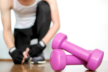 Fototapeta na wymiar Woman exercise by personal trainer at gym and then be tired. She sit on floor for rest that dumbbell in front of her. Women wearing sport shoes.
