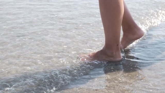 slow motion, female feet walk on the water by the sea, being swamped by the waves
