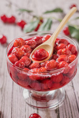 Bowl of cherry jam on the background of scattered berries and leaves on a table.