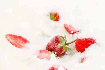 Red natural ripe strawberries falling into milk cream