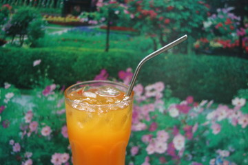 Fresh orange juice in crystal glass with stainless steel straw for drink on flower park background . Concept for reduce plastic pollution ,support green eco friendly products .