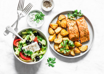 Mediterranean lunch table - baked lemon salmon with potatoes, greek salad, tzadziki sauce on light background, top view. Flat lay