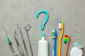 Toothpaste in the form of a question mark and many different and colored toothbrushes and dental floss, dental tool. Concept of how to choose the right toothbrush or how to brush your teeth