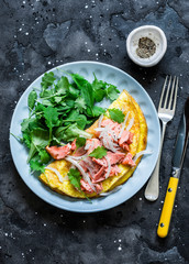 Omelet with green salad and baked salmon on a dark background, top view. Healthy breakfast, snack