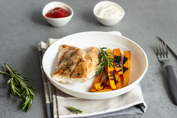 Grilled chicken or turkey fillets (steaks), roasted carrots and rosemary on a white plate, gray stone background.