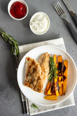 Grilled chicken or turkey fillets (steaks), roasted carrots and rosemary on a white plate, gray stone background.