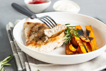 Grilled chicken or turkey fillets (steaks), roasted carrots and rosemary on a white plate, gray stone background.