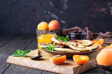 American pancakes or fritters with jam, fresh apricot and mint. Delicious dessert for breakfast. Wooden background, rustic style.  