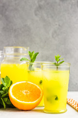Orange lemonade in glass with fresh orange and mint over light grey stone table. Refreshing summer drink. Cocktail bar background concept. Copy space.