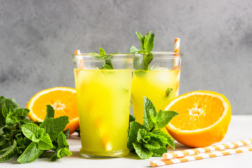 Fototapeta Orange lemonade in glass with fresh orange and mint over light grey stone table. Refreshing summer drink. Cocktail bar background concept. Copy space. obraz