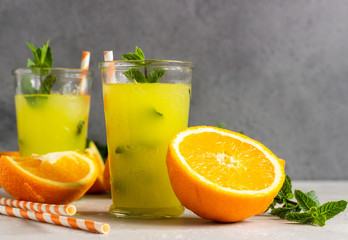 Orange lemonade in glass with fresh orange and mint over light grey stone table. Refreshing summer drink. Cocktail bar background concept. Copy space.