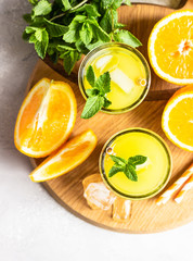 Orange lemonade in glass with fresh orange and mint over light grey stone table. Refreshing summer drink. Cocktail bar background concept. Copy space.