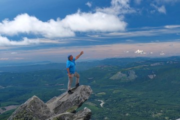 Man stretching  out  his arm and pointing to the horizon on mountain top. Victory pose. Mount Pilchuck State Park near Seattle. WA. United States of America.