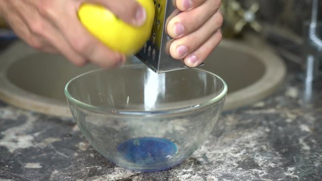 Man using a grater rubs lemon zest in a bowl