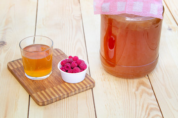 Kombucha in a jar on a light wooden background, a glass filled with kombuchey with raspberries.