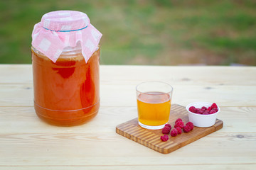 Glass jar with Kombucha, poured glass with Kombucha and raspberries in the summer garden.