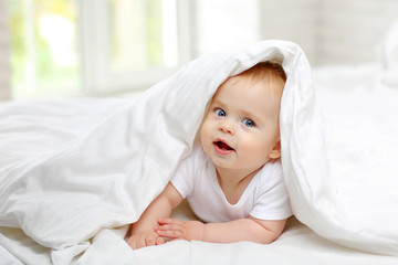 Portrait of a charming blue-eyed baby 7 months in bed in white clothes
