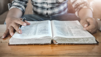 Naklejka premium Close up Bible or book with a man reading at home. christian concept.