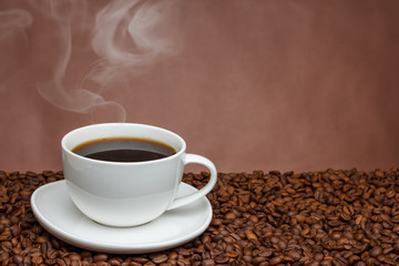 white cup of coffee with steam on a brown background on coffee beans